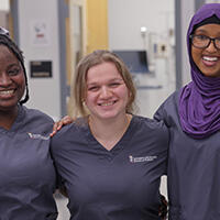 Three female students pose in a hospital in scrubs