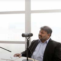 Dr. Dasgupta sitting behind a microphone in an open space in USG's building III