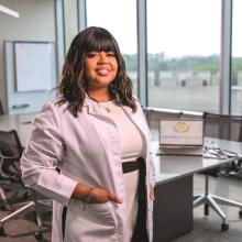 Black woman stands in white coat in a conference room
